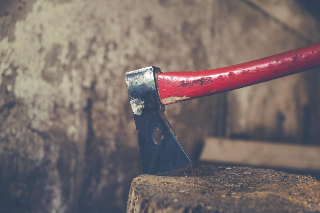 Detailed view of a red handled axe embedded in a wooden stump, outdoors.